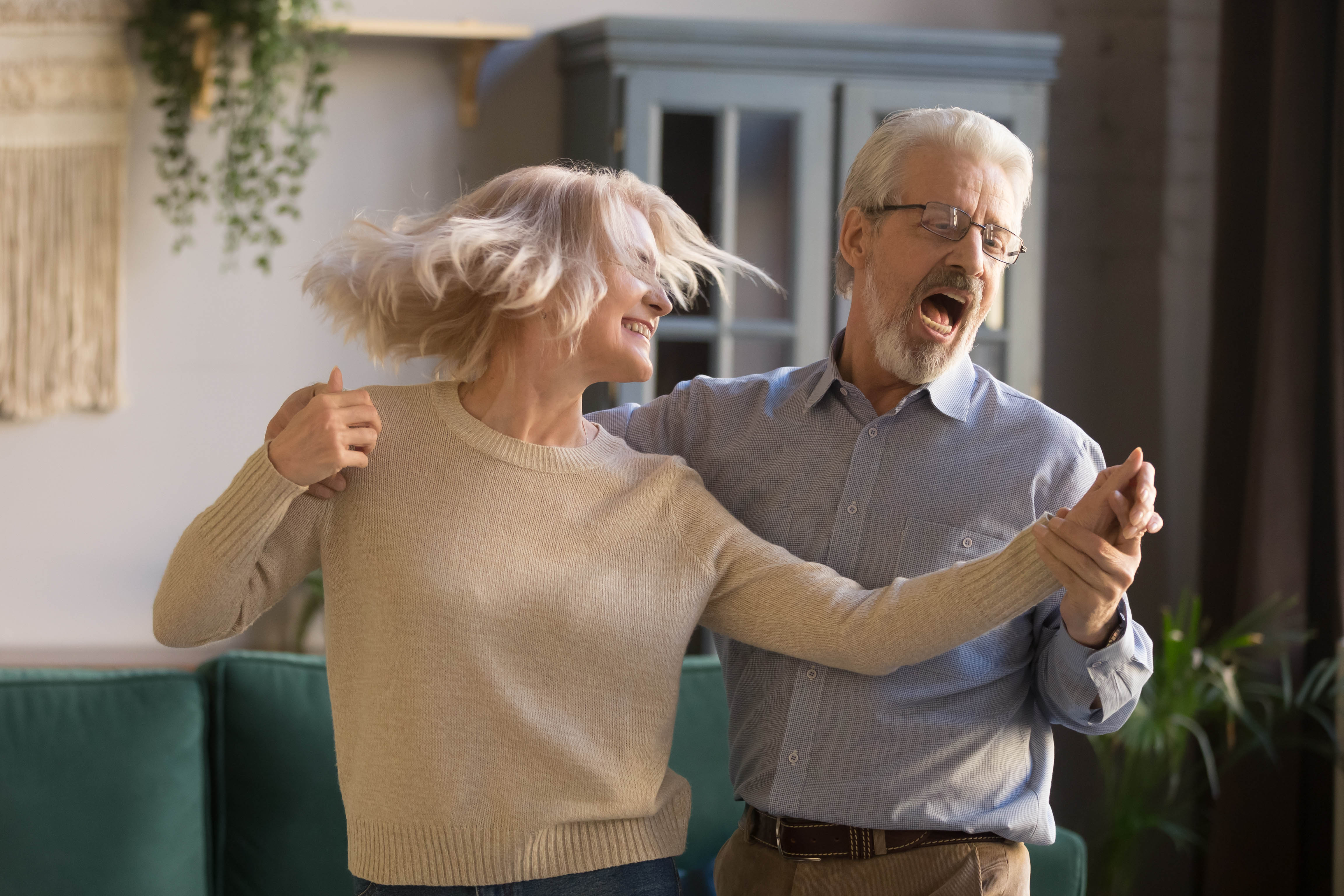 Older couple dancing, laughing, and singing in their living room